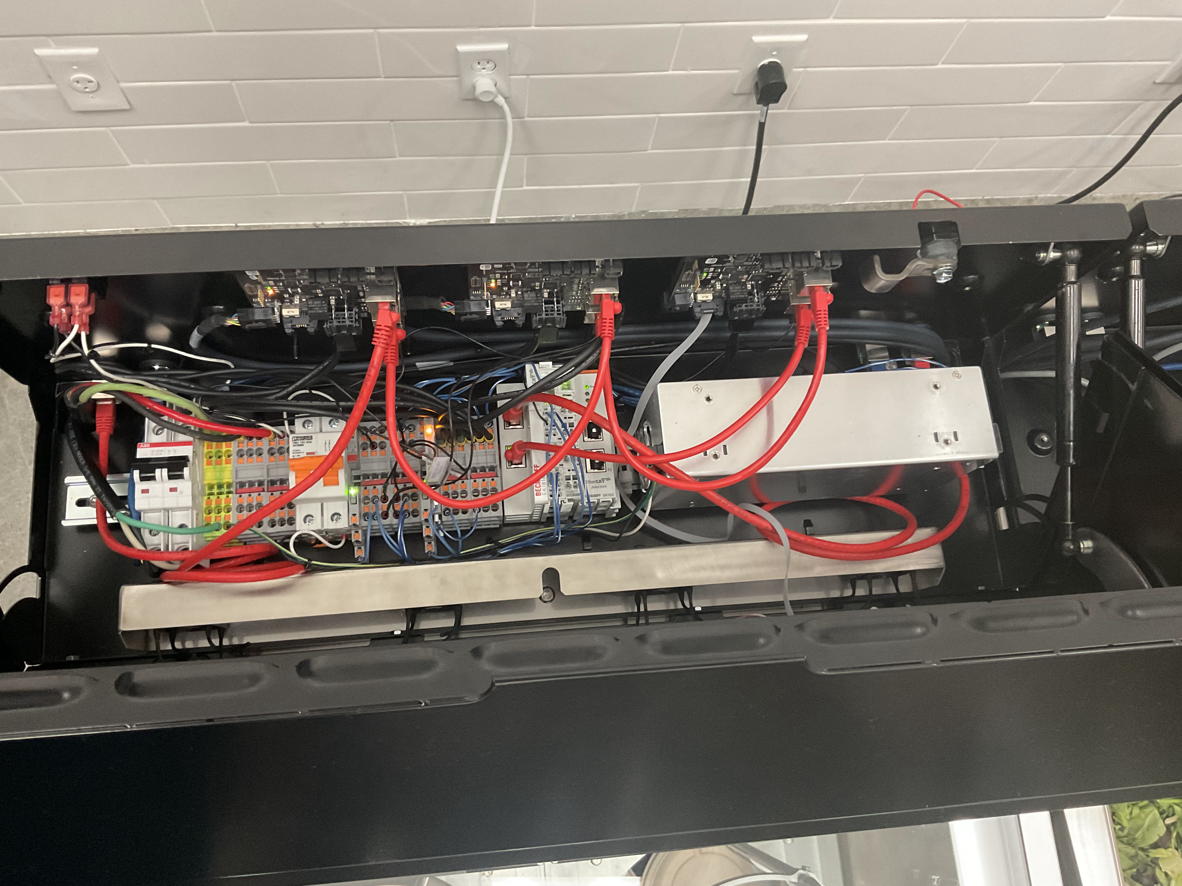 An open enclosure with circuit boards, terminal blocks and red and gray cables.