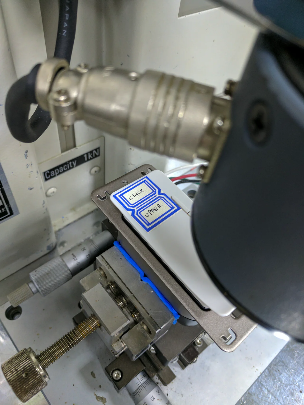 Close view of an instrumented press above a control module mounted on a fixture.