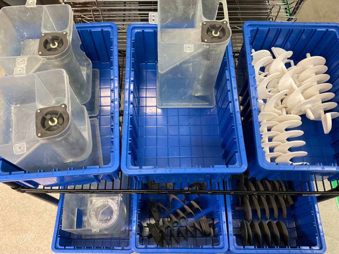 Translucent containers and separate helical dispenser parts arranged in blue wash racks.